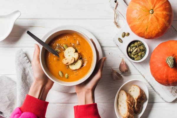 Cropped image of woman holding plate with homemade pumpkin cream soup with seeds and rusks on table — Stock Photo