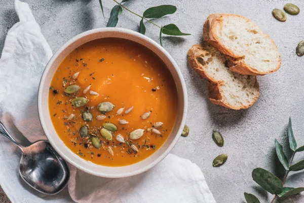 Top view of bowl with pumpkin cream soup with seeds and bread on table — Stock Photo