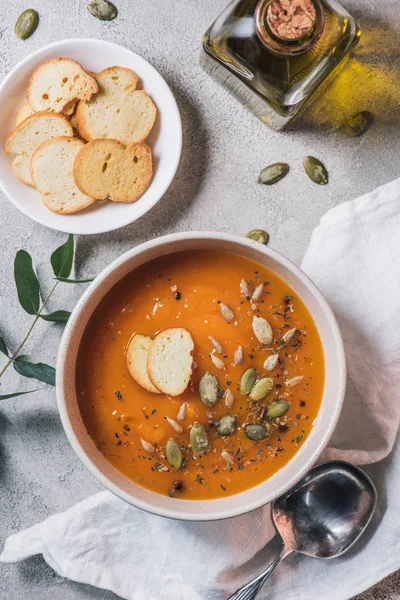 Top view of rusks, bottle of olive oil and bowl with pumpkin cream soup with seeds on table — Stock Photo