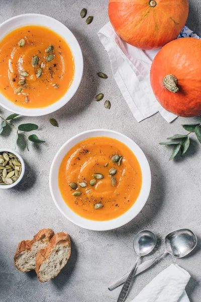 Top view of plates with homemade pumpkin soup, rusks and pumpkins on table — Stock Photo