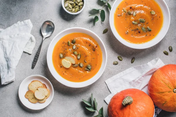 Elevated view of pumpkins, rusks and plates with pumpkin cream soup on table — Stock Photo