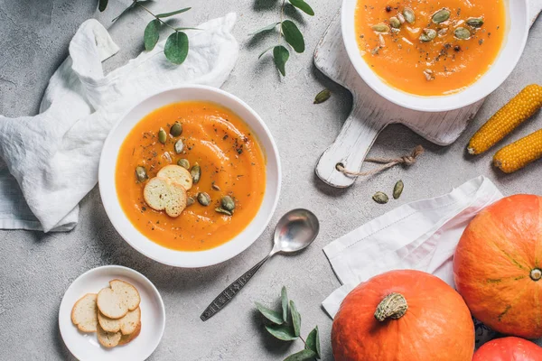 Vue de dessus des épis de maïs, citrouilles, biscottes et assiettes avec soupe à la crème de citrouille sur la table — Photo de stock