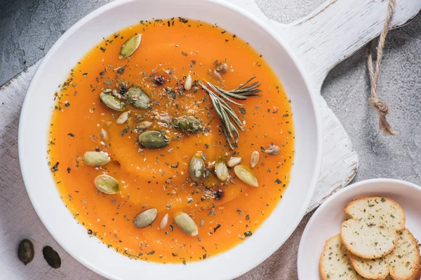 Top view of rusks and plate with pumpkin soup with seeds on table — Stock Photo