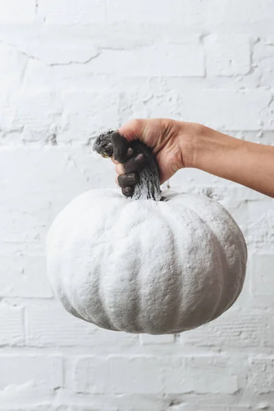 Cropped shot of woman holding white painted halloween pumpkin in front of white brick wall — Stock Photo