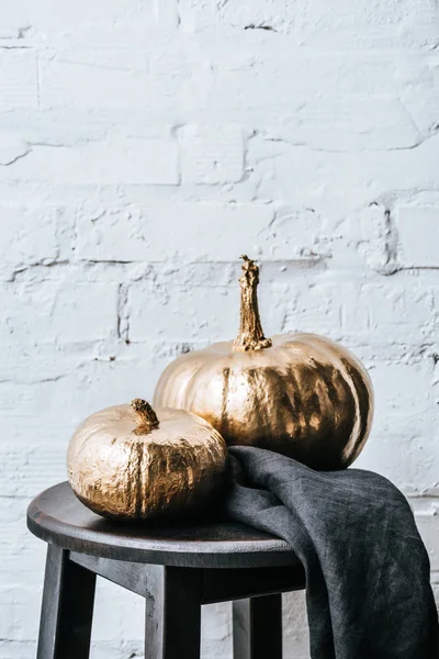 Primer plano de dos calabazas de halloween pintadas en oro metálico delante de la pared de ladrillo blanco - foto de stock