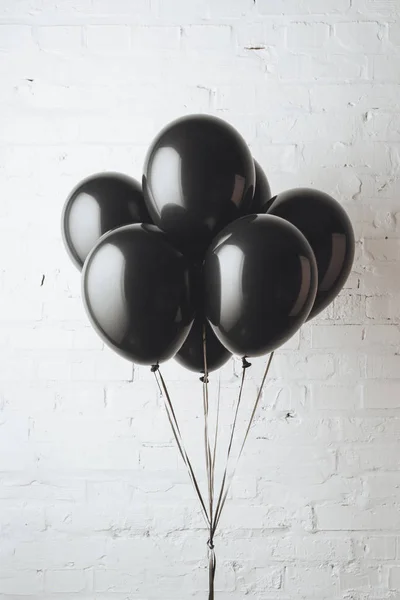 Bunch of black balloons on ribbons in front of white brick wall — Stock Photo