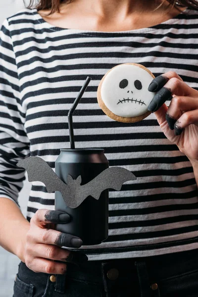 Cropped shot of woman holding black can of soda and hallooween cookie — Stock Photo