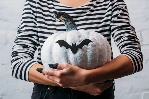 Cropped shot of woman holding white painted halloween pumpkin with bat sticker — Stock Photo