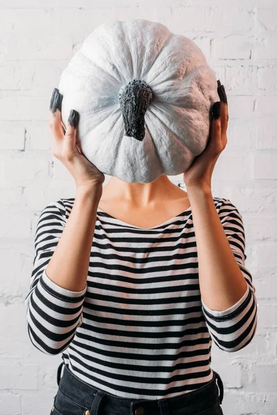 Femme tenant la citrouille d'Halloween peinte en blanc devant la tête — Photo de stock