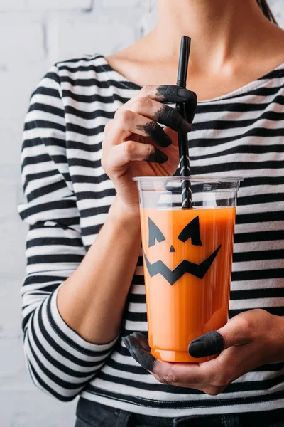 Cropped shot of woman holding glass of pumpkin juice with jacks face, halloween concept — Stock Photo