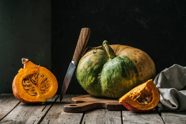 Vista ravvicinata della composizione alimentare con zucche, coltello e tagliere su superficie in legno su fondo scuro — Foto stock