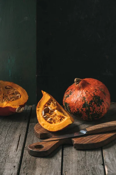 Close up view of raw cut pumpkins arranged on cutting board with knife on dark backdrop — Stock Photo