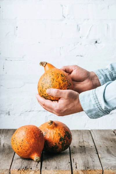 Vue partielle de l'homme et citrouilles mûres sur plateau en bois et fond de mur de briques blanches — Photo de stock