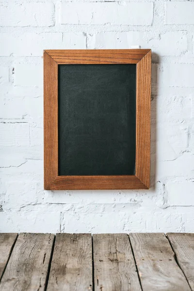 Close up view of blank chalkboard on white brick wall and wooden planks surface — Stock Photo