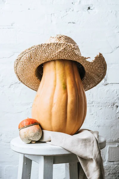 Close up view of pumpkins and straw hat on wooden chair with linen on white brick wall background — Stock Photo