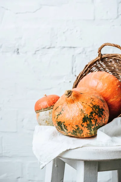Close up view of pumpkins and basket on chair with linen on white brick wall background — Stock Photo