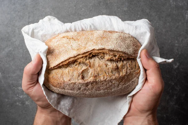 Schnappschuss eines Mannes mit Brotlaib in der Hand vor grauem Hintergrund — Stockfoto
