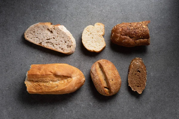 Flat lay with pieces of various bread on grey tabletop — Stock Photo