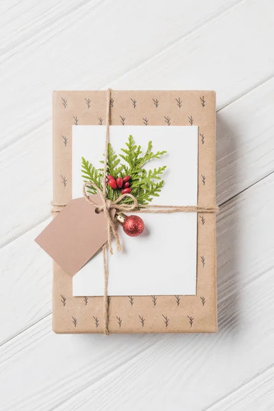 Vista elevada de la caja de regalo decorada con rama perenne y adornos de Navidad en la mesa de madera - foto de stock