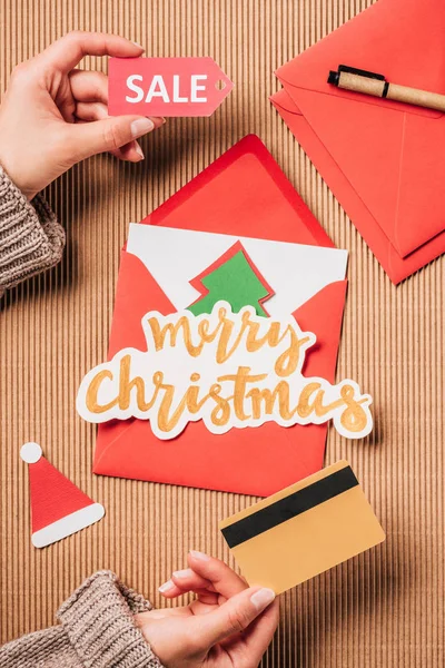 Cropped image of woman holding sale sign and credit card over surface with greeting envelope on surface — Stock Photo