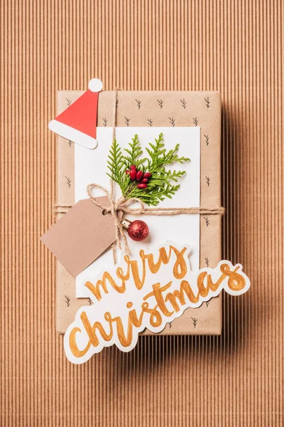 Flat lay with gift box with baubles, evergreen branch and merry christmas lettering on surface — Stock Photo