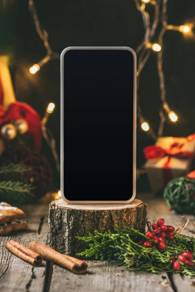 Смартфон с чистым экраном на деревянном пне с рождественским декором — стоковое фото