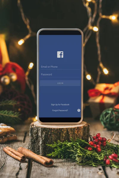 Smartphone with facebook app on wooden stump with christmas decoration — Stock Photo