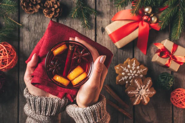 Vista ritagliata della donna che tiene il bicchiere con il vino speziato caldo di Natale su sfondo di legno — Foto stock