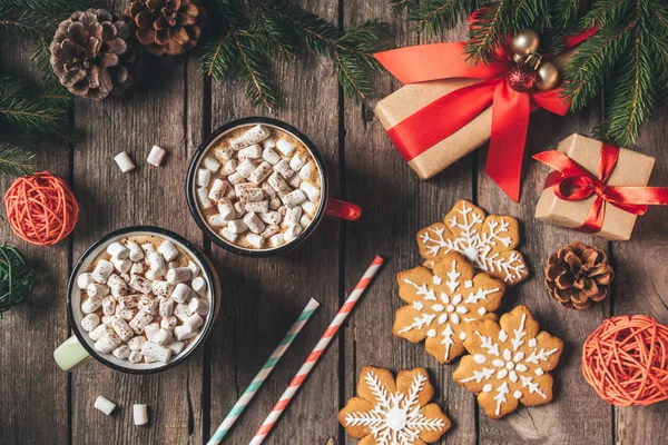 Flat lay with gingerbread, christmas gifts and cups of cocoa with marshmallows on wooden background with fir tree — Stock Photo