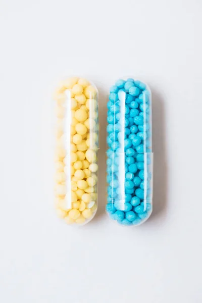Вид сверху на голубые и желтые медицинские капсулы на белом — стоковое фото