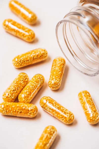 Close-up shot of yellow medical capsules spilled from jar on white — Stock Photo