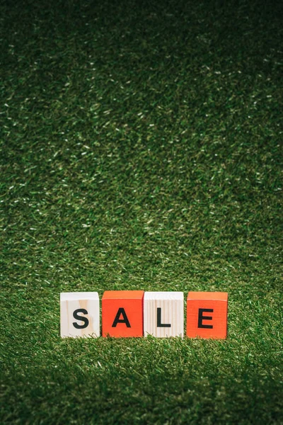 Rote und hölzerne Buchstabenwürfel mit Verkaufsschild auf grünem Gras — Stockfoto
