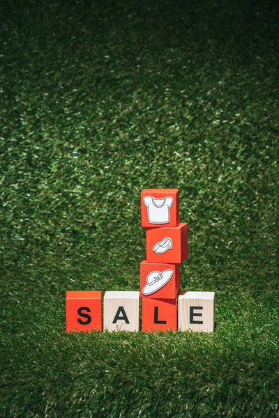 Red and wooden alphabet cubes with sale sign and clothes on green grass for black friday — Stock Photo