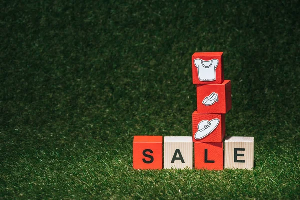 Красные и деревянные кубики алфавита с табличкой продажи и одеждой на зеленой траве — стоковое фото