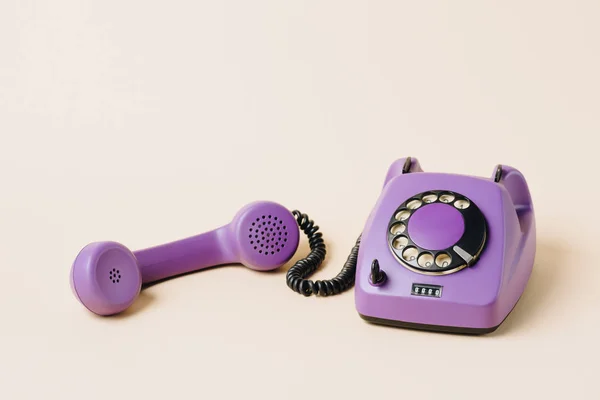Фиолетовый ретро-телефон с трубкой на бежевом — стоковое фото