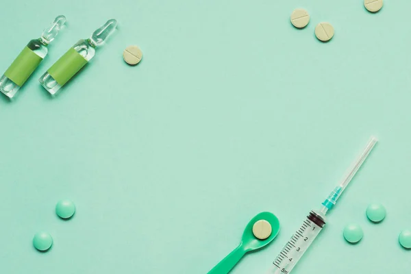 Вид на ампулы с лекарствами, таблетками и шприцем на зеленом фоне — стоковое фото