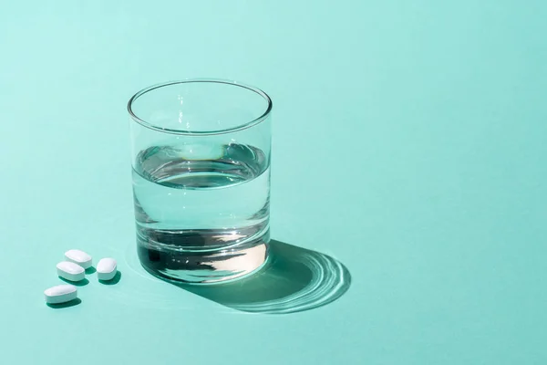 Primer plano vista de vaso de agua y píldoras médicas en verde - foto de stock