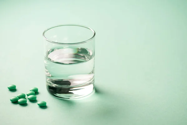 Close-up view of glass of water and medical tablets on green — Stock Photo
