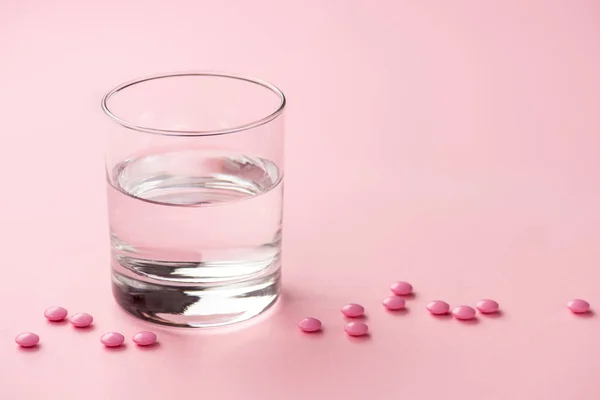 Крупним планом склянка води і медичних таблеток на рожевому — стокове фото