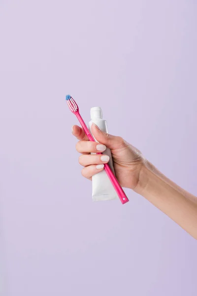 Tiro recortado de mujer sosteniendo cepillo de dientes y tubo de pasta aislado en púrpura - foto de stock