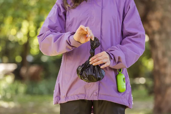 Recortado disparo de mujer joven sosteniendo la bolsa de basura mientras limpia después de mascota en el parque - foto de stock