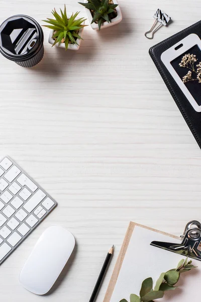 Tendido plano con plantas en maceta, taza de café de papel, ratón de computadora y teclado en la mesa en la oficina - foto de stock