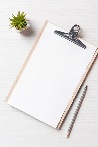 Vista elevada del lugar de trabajo con portapapeles en blanco, planta en maceta y lápiz en la oficina, concepto minimalista - foto de stock