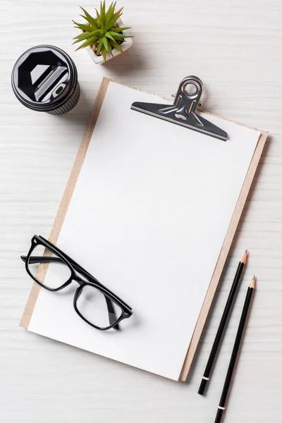 Top view of paper coffee cup, pencils, potted plant and empty clipboard at table in office — Stock Photo