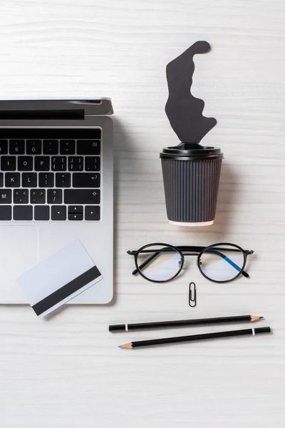 Flat lay com laptop, cartão de crédito, óculos e xícara de café descartável à mesa no escritório — Fotografia de Stock