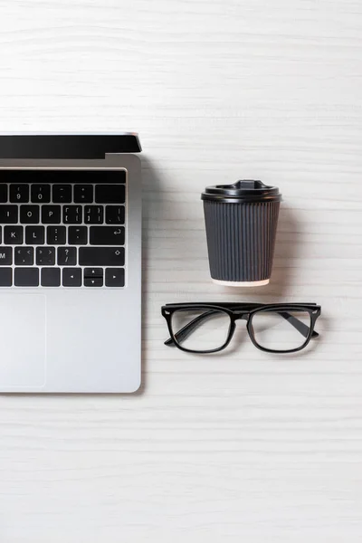 Vista superior do portátil arranjado, óculos e xícara de café de papel na mesa no escritório, conceito minimalista — Fotografia de Stock