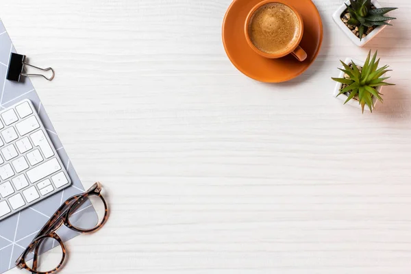 Верхний вид чашки кофе, очки, горшки растений и клавиатуры компьютера за столом в офисе — стоковое фото