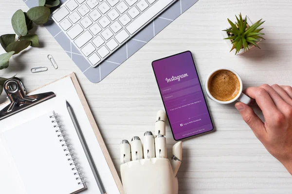Обрезанный образ бизнесмена с протезной рукой с помощью смартфона с YouTube на экране за столом с чашкой кофе в офисе — стоковое фото