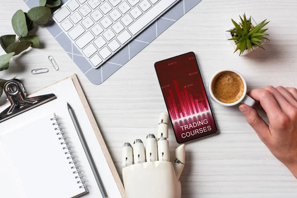 Immagine ritagliata di uomo d'affari con braccio protesi utilizzando smartphone con corsi di trading sullo schermo a tavola con tazza di caffè in ufficio — Foto stock