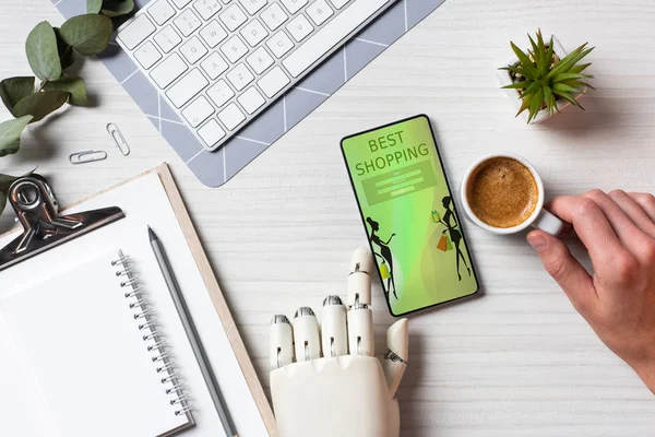 Teilbild des Geschäftsmannes mit Prothesenarm am Smartphone mit besten Einkäufen auf dem Bildschirm am Tisch mit Kaffeetasse im Büro — Stockfoto